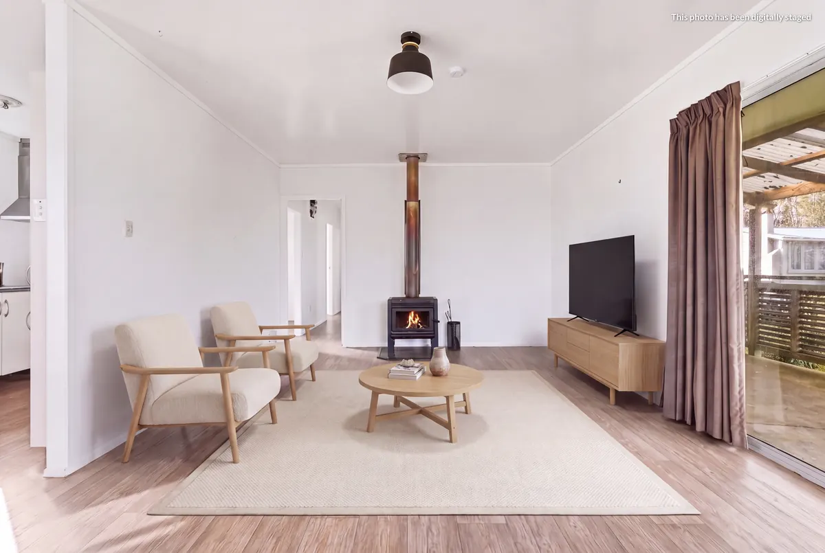 Staged lounge at 76 Takahe Road looking toward the wood burner, with the digitally staged label top right
